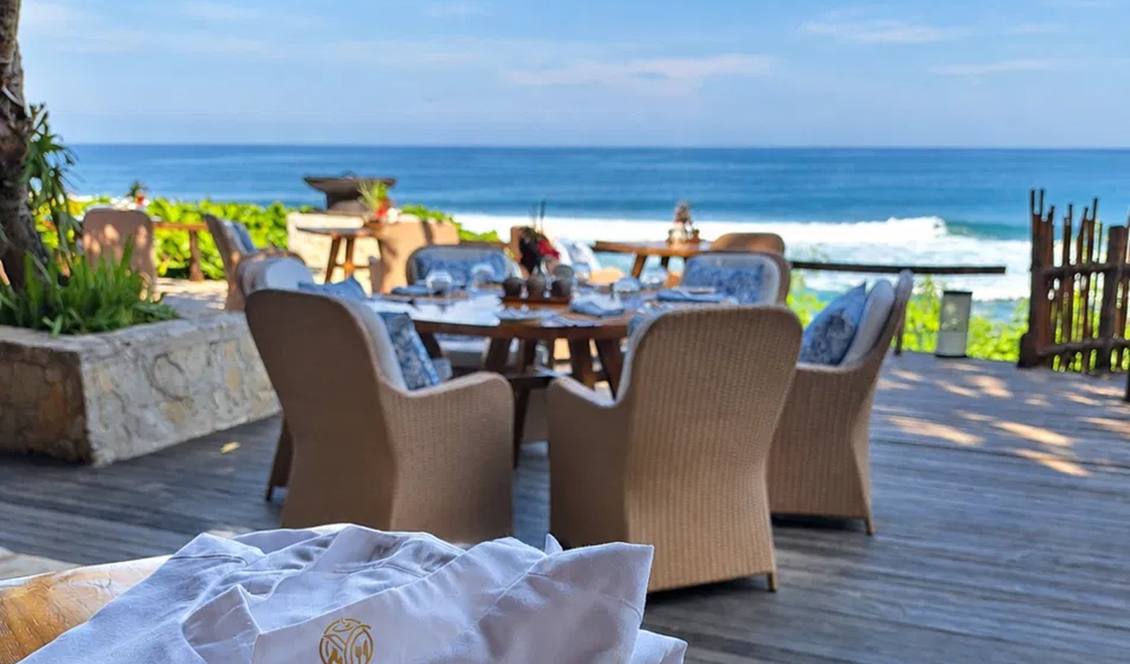 A Yunic chef's jacket with the gold monogram on a beachfront dining table, the ocean behind